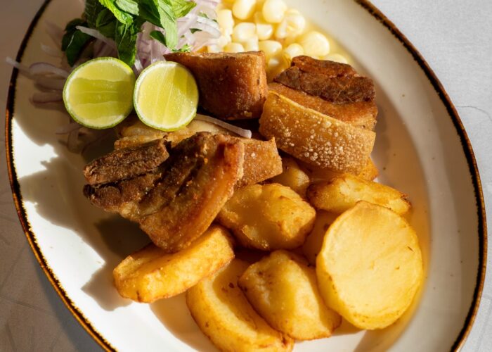 Chicharron cusqueno with mote and potato Chicharron cusqueno served with mote, potato and salsa criolla in Cusco, Peru